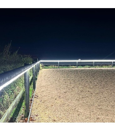 Sfeervolle LED-verlichting langs de omtrek van een paardenrijbak bij avond.